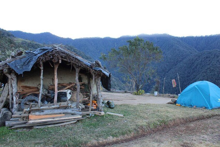 A rustic hut with a blue tent nearby, surrounded by a mountainous landscape. 3