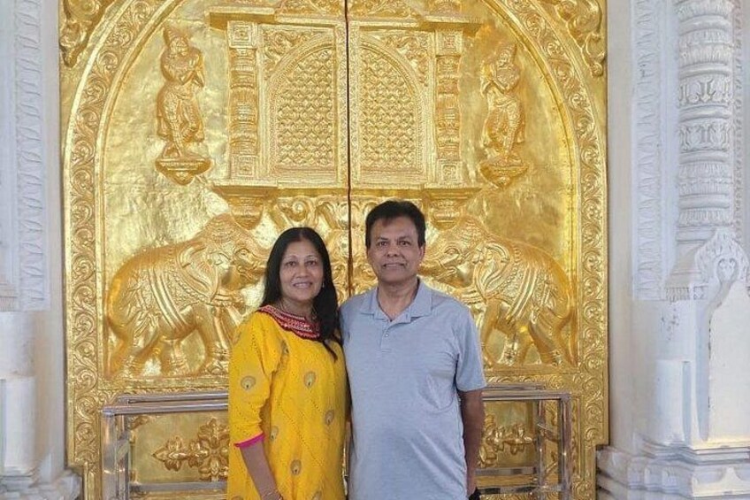 A couple standing in front of a golden ornate door with intricate designs and figures. 5