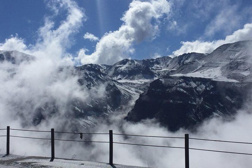 A mountain range with snow-covered peaks and a fence in the foreground. 1