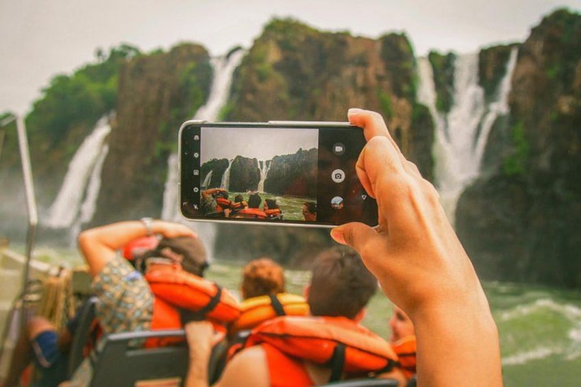 Una persona che fotografa una cascata con una barca e passeggeri a bordo. 4