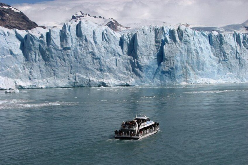 A boat on calm waters with a large glacier in the background. 1
