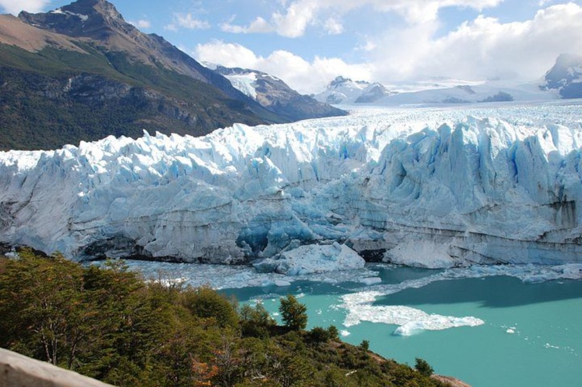 A glacier with turquoise water at its base, surrounded by mountains and trees. 4