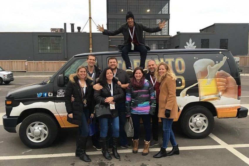 A group of people posing in front of a van with a beer advertisement. 5