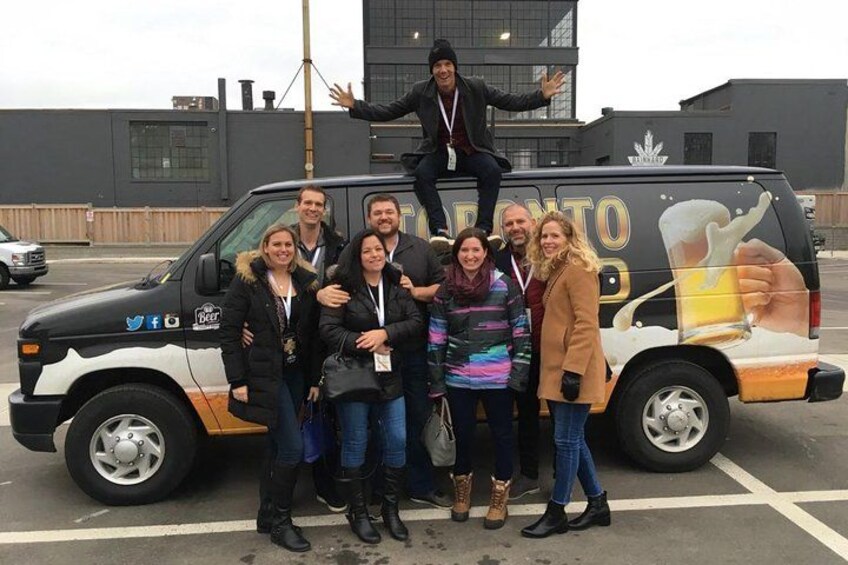 A group of people standing in front of a van with a beer advertisement. 2