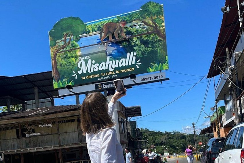 A woman taking a photo of a billboard advertising 'Misahualli' with a bear and a waterfall. 5