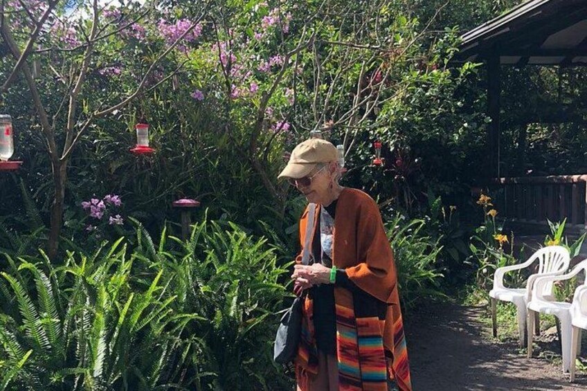 An elderly person in a garden with ferns, flowering plants, and hanging lanterns. 3