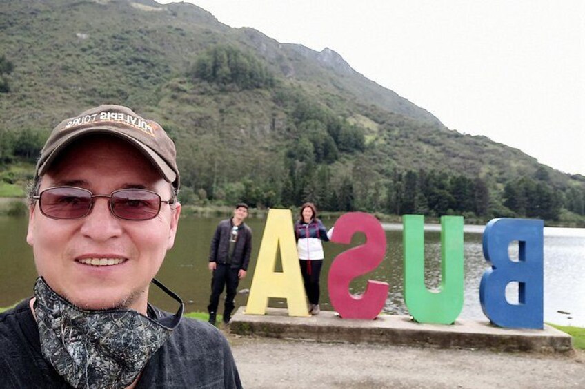 Une personne se tient devant de grandes lettres colorées qui épellent le mot « BASU », au bord d’un lac, avec des montagnes en arrière-plan. 4