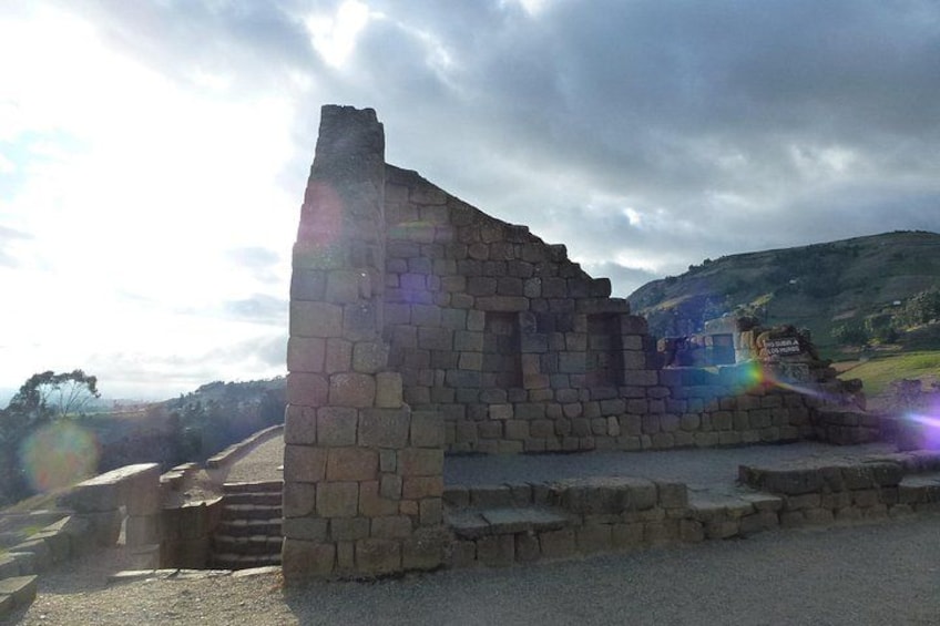 A stone structure with steps leading up to it, set against a hilly landscape. 5