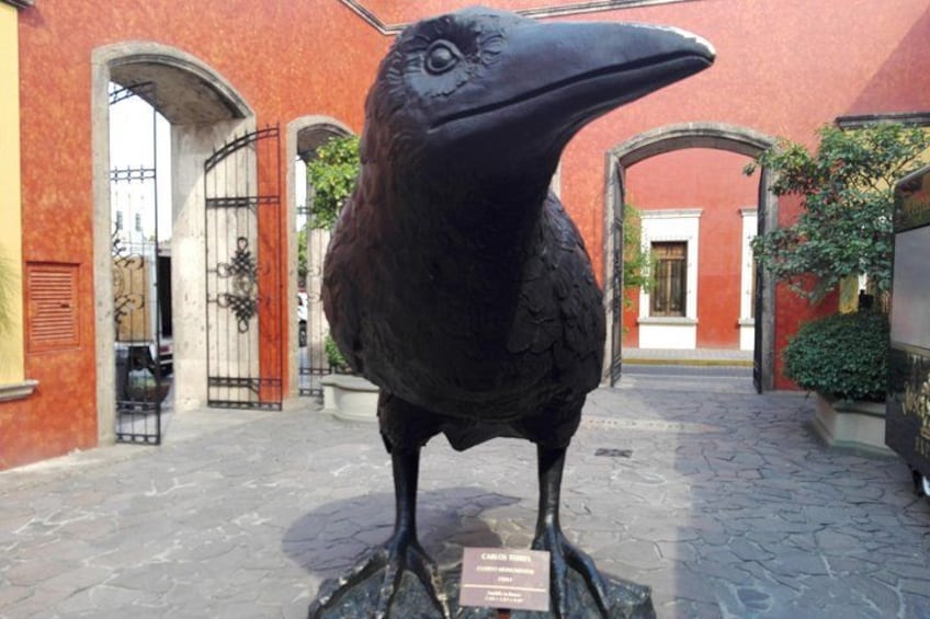 A large bird sculpture in a courtyard with red walls and arched doorways. 3