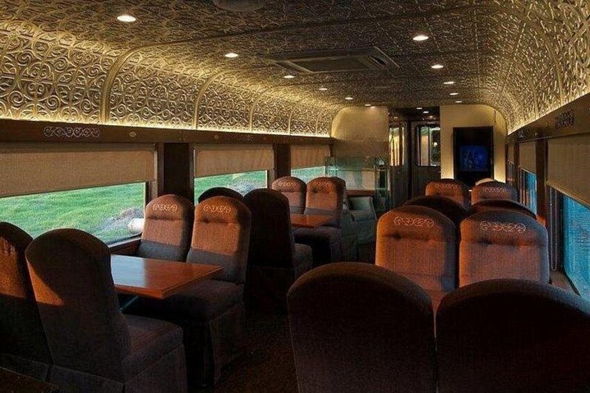 Interior de un tren con techo estampado, hileras de asientos y una pantalla de televisión. 5