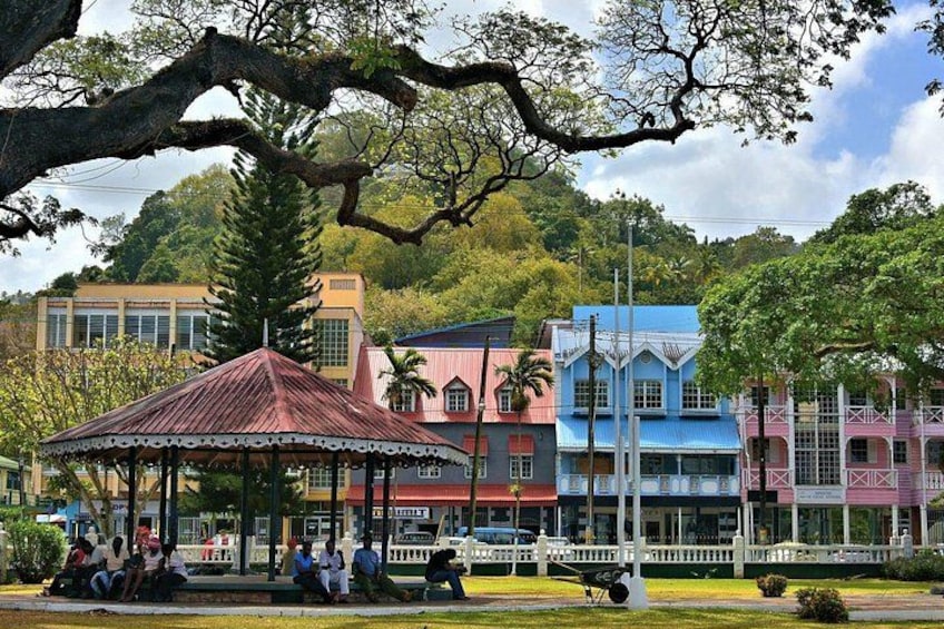 A gazebo in a park with colorful buildings in the background. 1