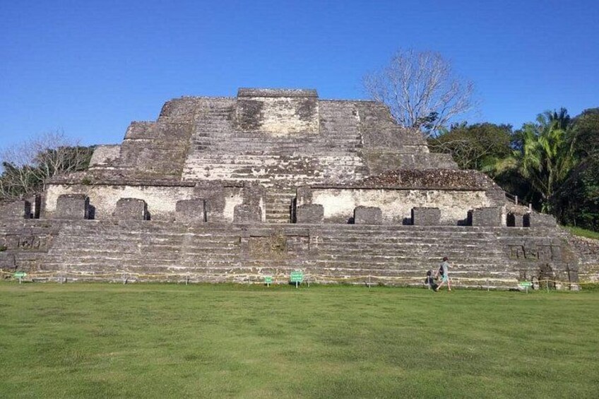 A large ancient pyramid with a stepped structure, surrounded by a grassy area and palm trees. 1
