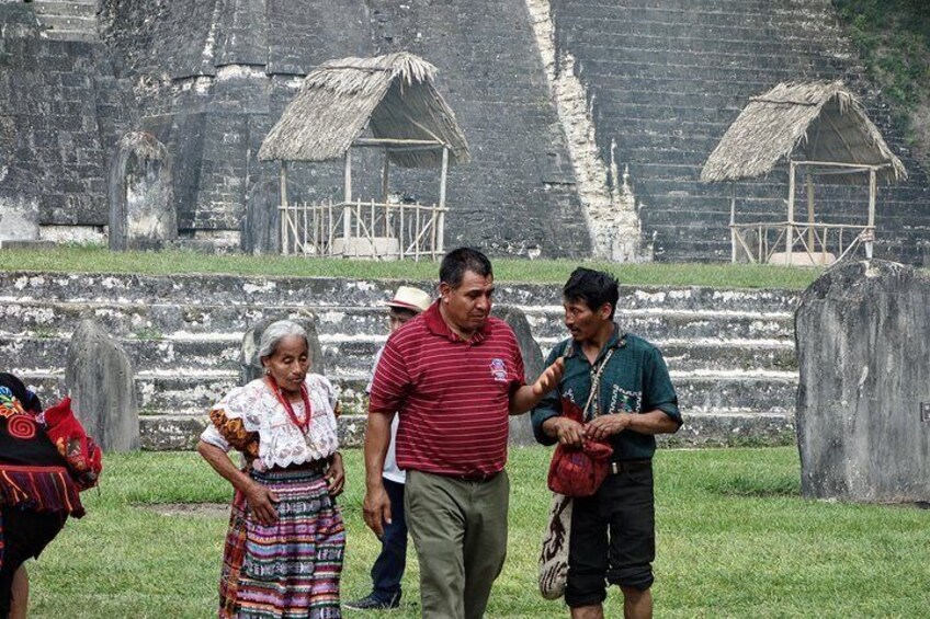 A group of people standing in front of ancient ruins with stepped structures and thatched-roof huts. 5