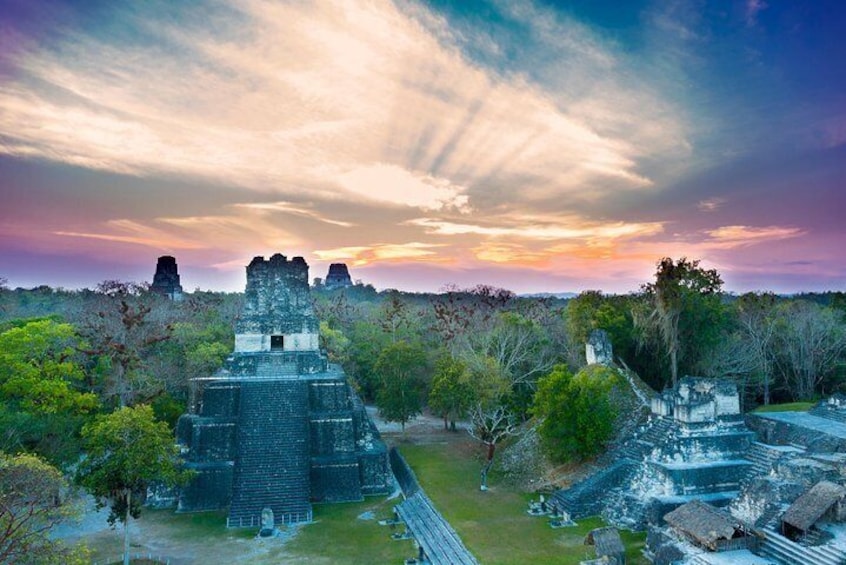 A pyramid-like structure surrounded by trees and ruins at sunset. 2