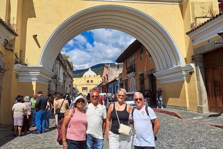 A cobblestone street with an arched entrance, historic buildings, and a mountainous backdrop. 2
