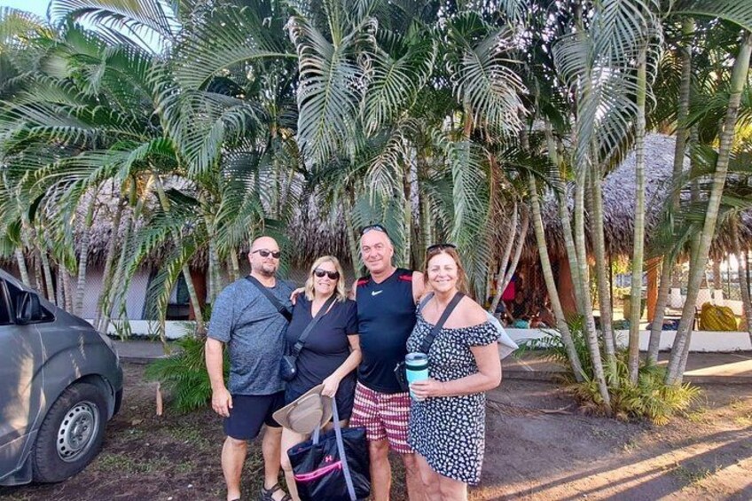 A group of people standing in a tropical setting with palm trees and a parked car. 4