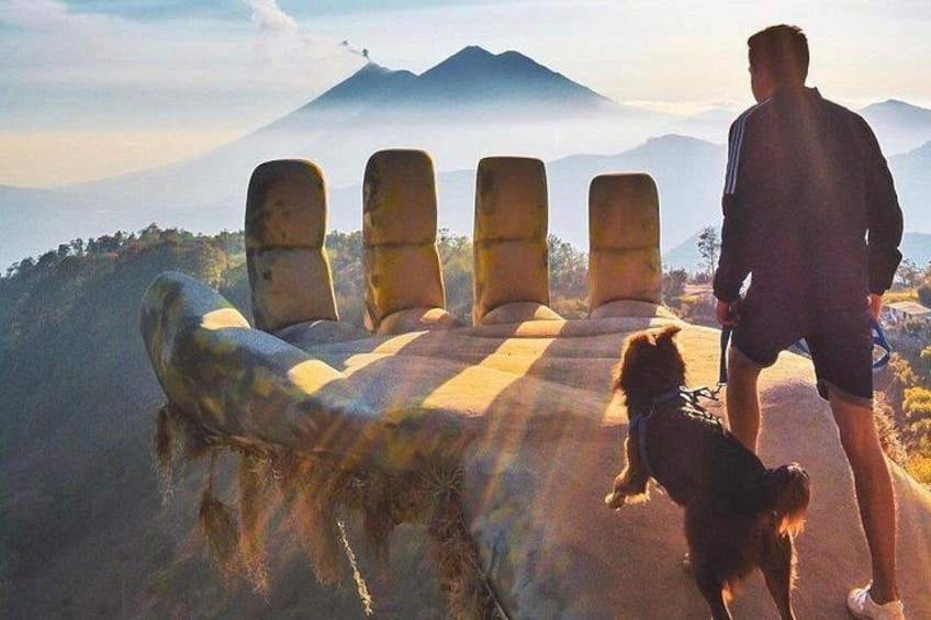 Una persona paseando un perro por un sendero con bancos de piedra, con vistas a un paisaje montañoso. 1