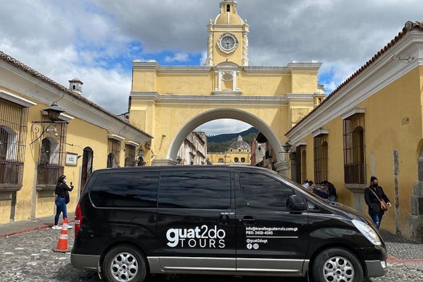 Una camioneta negra con la leyenda 'guatamala tours' estacionada frente a un edificio histórico con una torre de reloj. 2