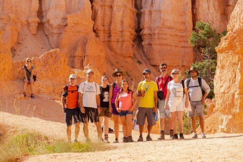 Un gruppo di escursionisti su un sentiero sterrato con formazioni rocciose rosse sullo sfondo. 2