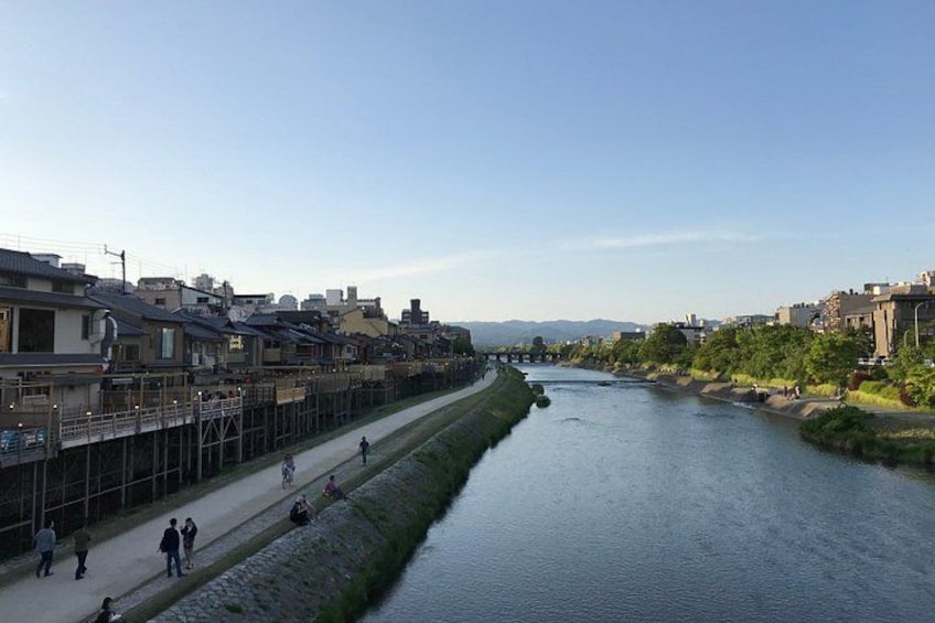 A river with a walkway alongside it, buildings on one side, and greenery on the other. 2