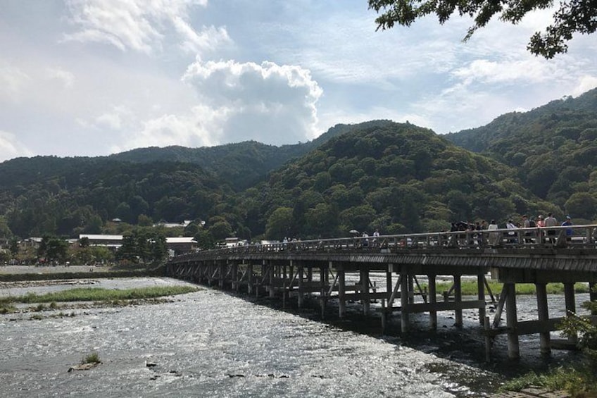 A wooden bridge over a river with people walking on it, surrounded by lush green hills. 4