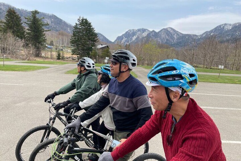 A group of cyclists on a paved road with mountains in the background. 4