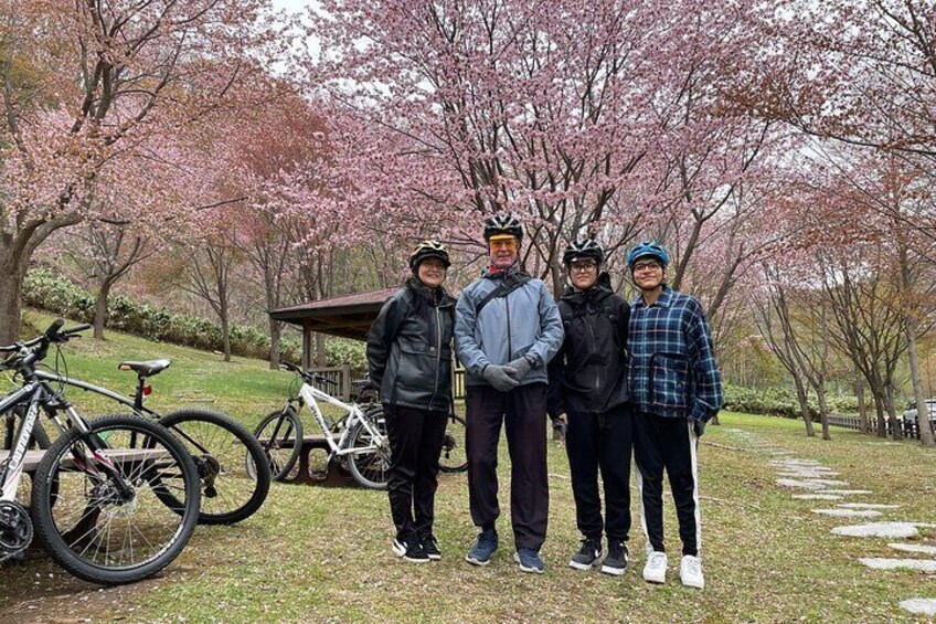 A group of people standing in a park with cherry blossoms and bicycles. 3