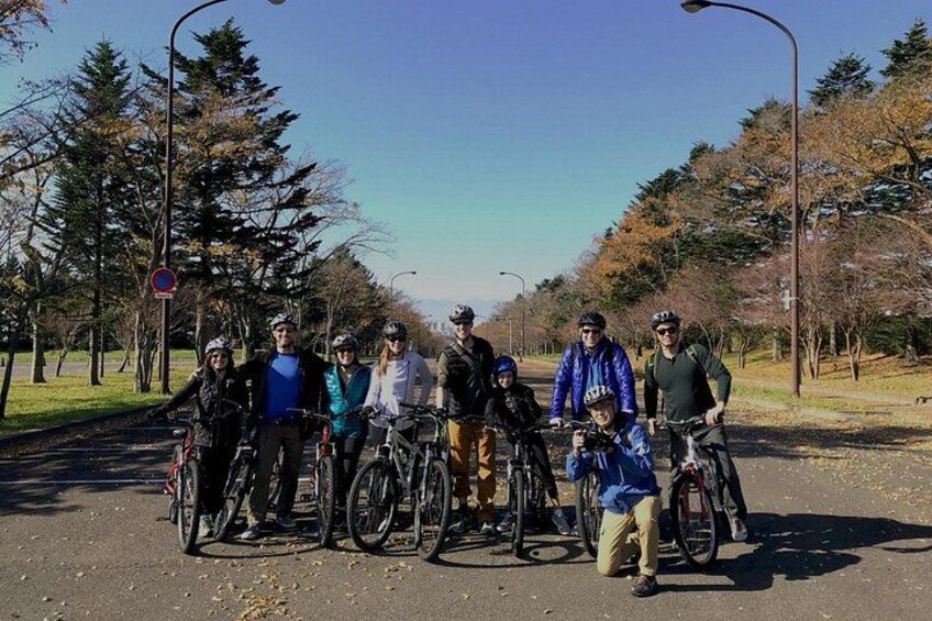 Un grupo de ciclistas en un camino pavimentado con árboles y farolas al fondo. 2