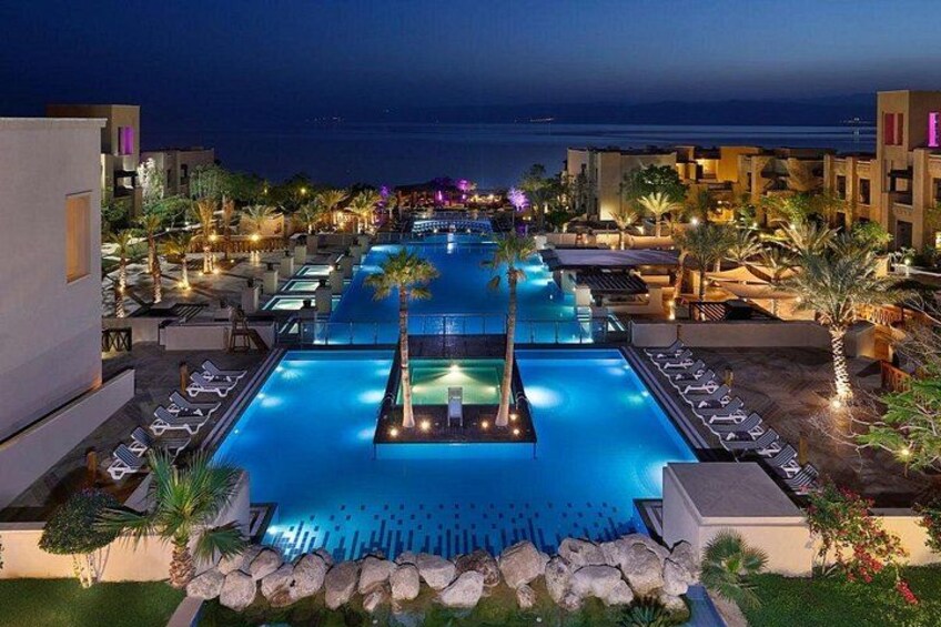 A nighttime swimming pool with lounge chairs and palm trees. 1