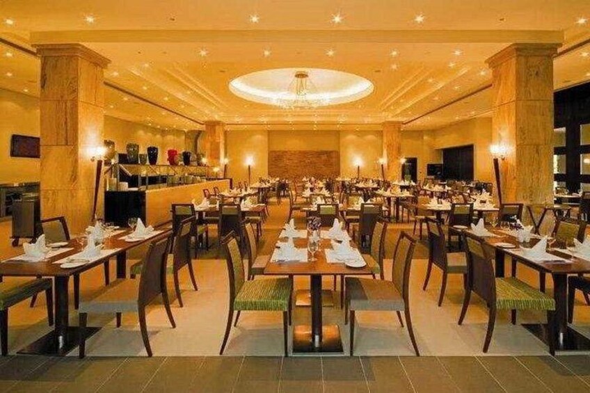 A large dining hall with multiple tables and chairs, a central chandelier, and a bar area. 5