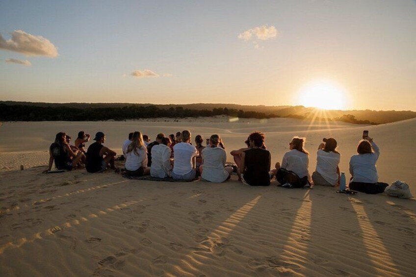 Un groupe de personnes assises sur une plage de sable au coucher du soleil. 1