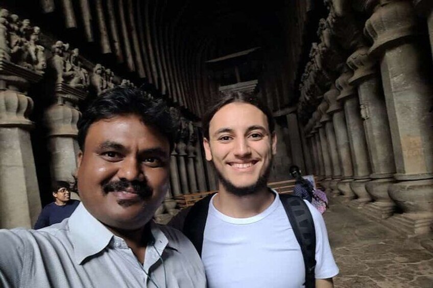 Two people standing in a historical building with detailed stone carvings and columns. 1