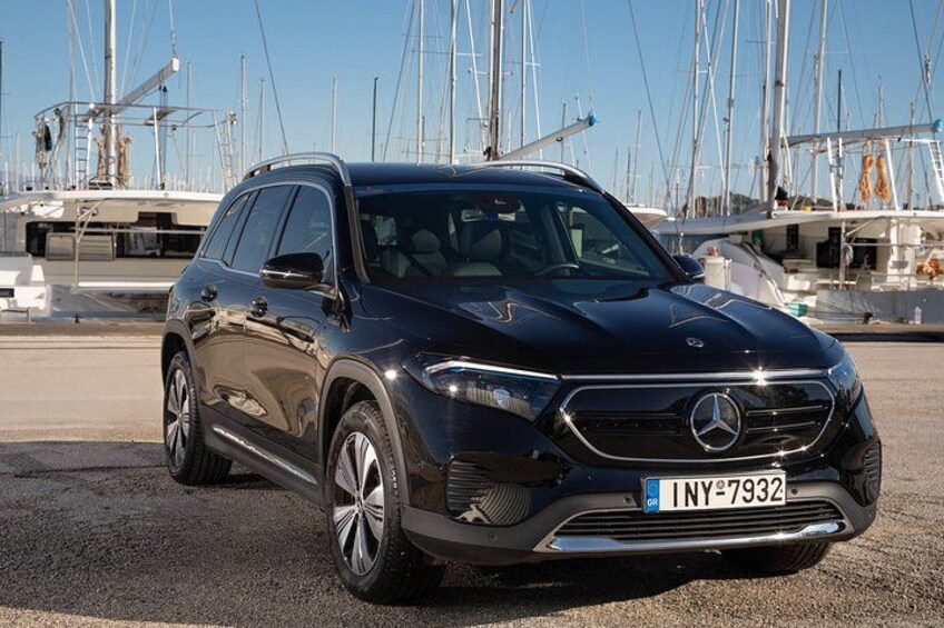 Un SUV Mercedes-Benz nero parcheggiato in una marina, con barche a vela sullo sfondo. 5