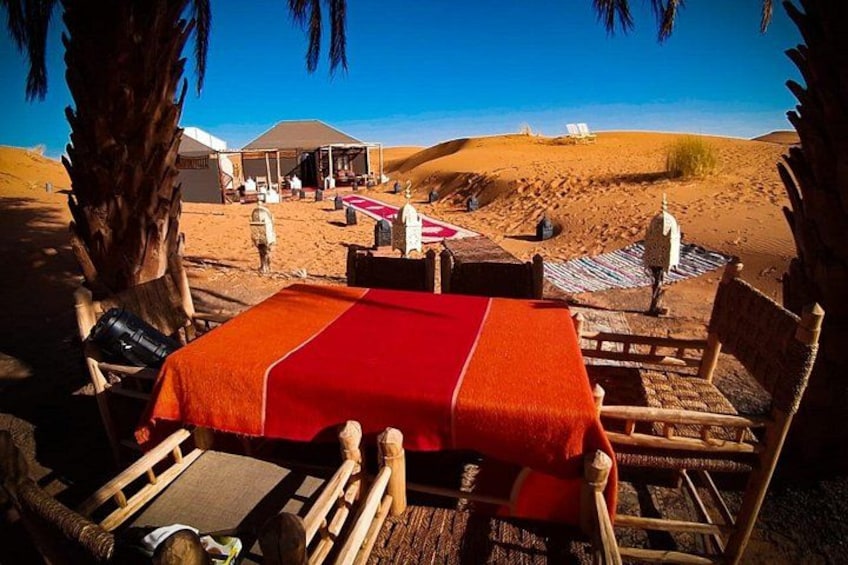 Un campement dans le désert, avec une nappe rouge, des chaises en bois et une tente en arrière-plan. 2