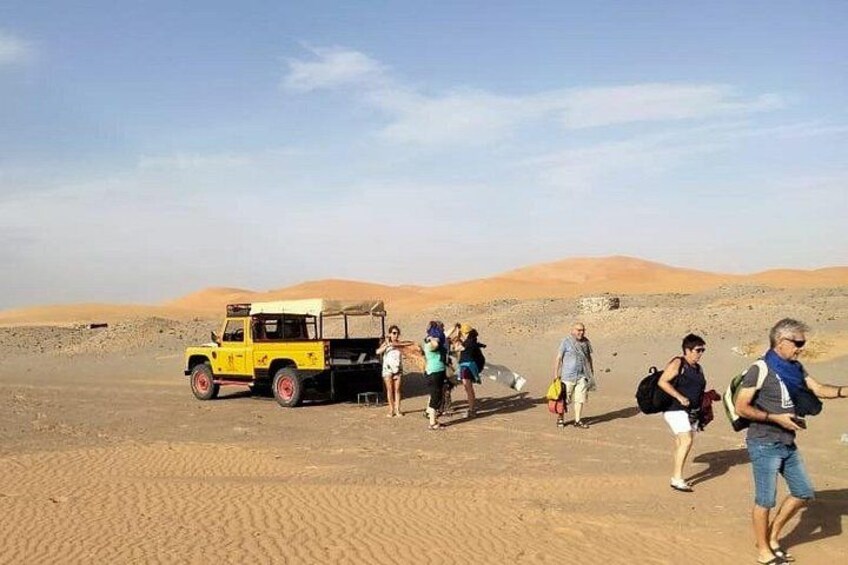 Un groupe de personnes marchant dans un désert, avec un véhicule jaune. 3