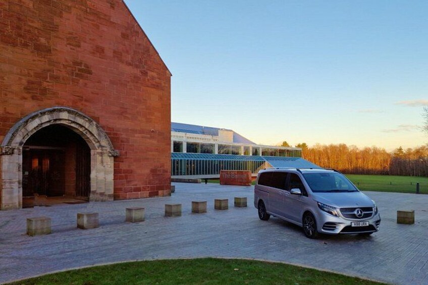 A silver van parked in front of a red brick building with a modern glass structure in the background. 2