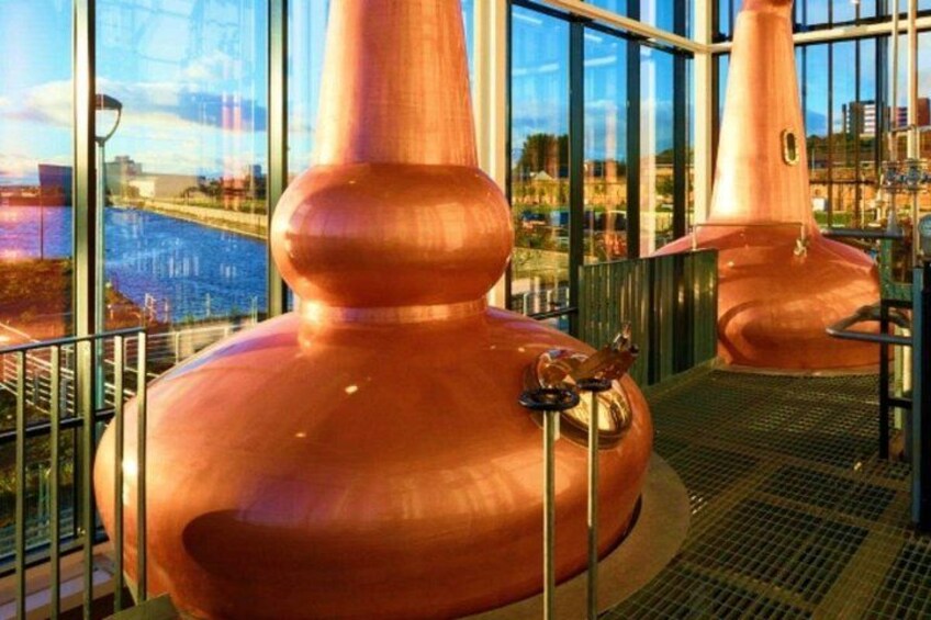 Large copper distillation columns in a modern industrial setting with a view of a river and buildings in the background. 5