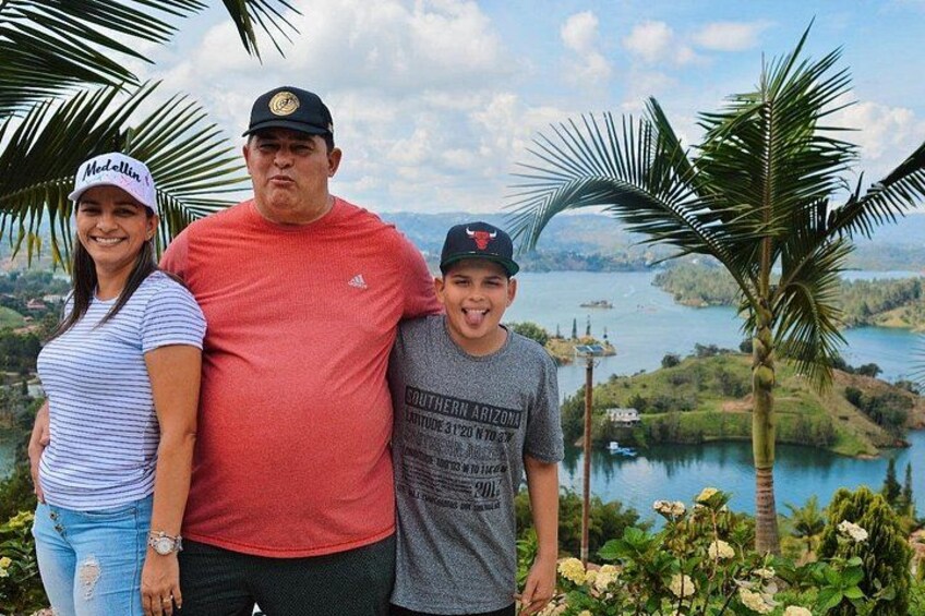 A family standing in front of a scenic view of a lake with palm trees and a mountainous landscape. 3