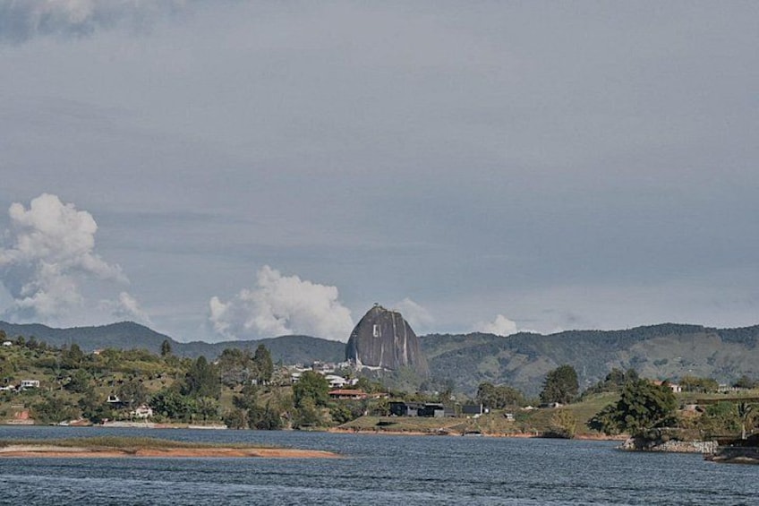 Una gran formación rocosa cerca de una masa de agua, con colinas al fondo. 2