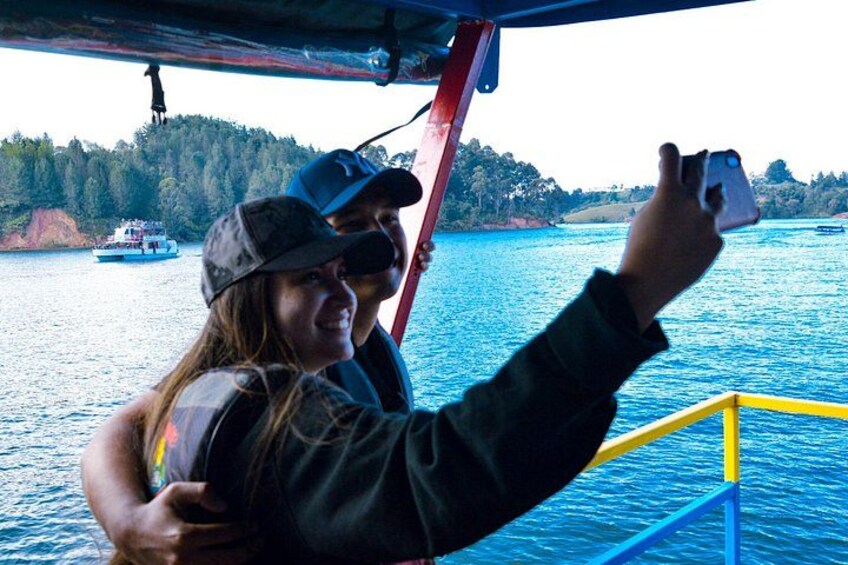 A person taking a selfie with a scenic view of a body of water and a forested hill in the background. 5
