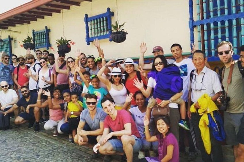 Un grupo de personas posando frente a un edificio con contraventanas azules y plantas colgantes. 5