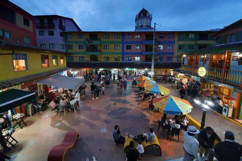 A bustling square with colorful buildings, outdoor seating, and a prominent clock tower. 5