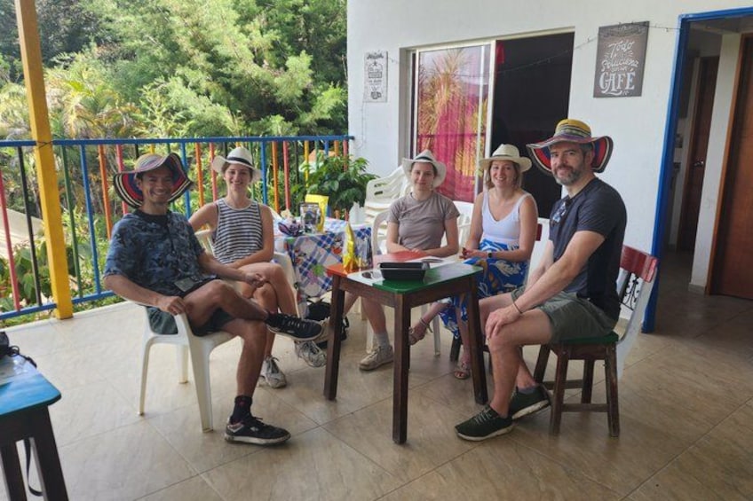 Een groep mensen zit aan een tafel op een veranda, met uitzicht op groen. 4