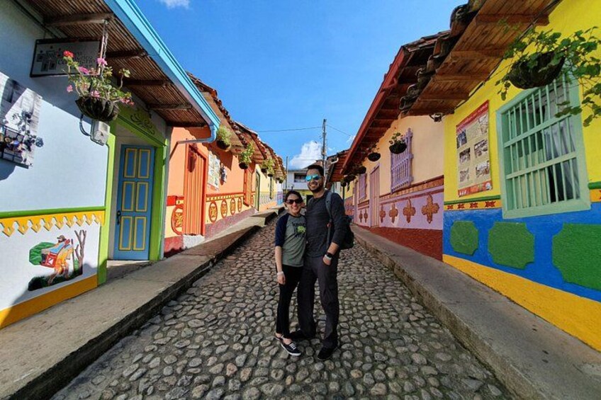 A cobblestone street lined with colorful buildings, a person standing in the middle, and a clear blue sky. 2