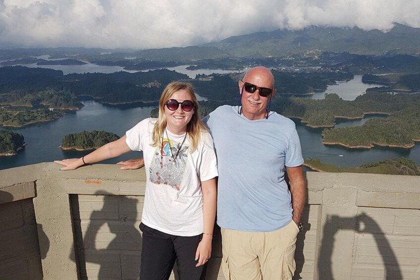 Two people standing on a concrete ledge overlooking a lake and forested landscape. 2