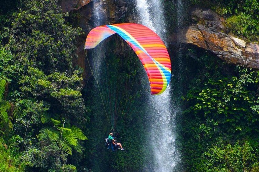 A person paragliding over a waterfall with lush greenery around. 1