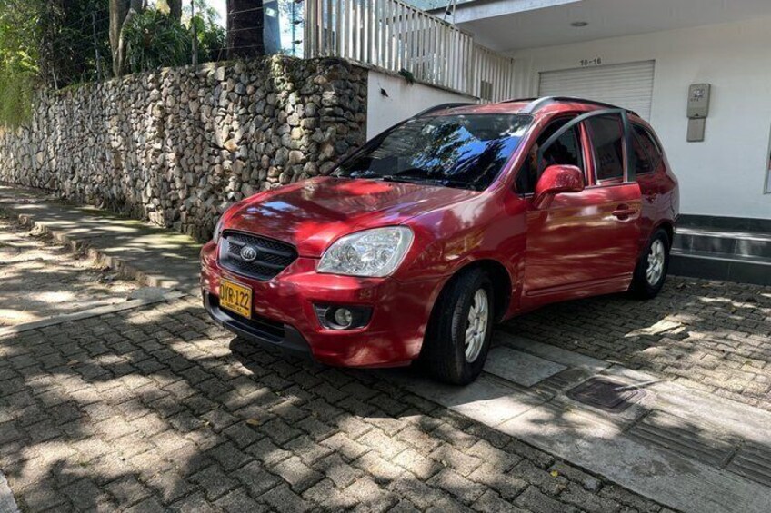 Une voiture rouge est garée sur une allée pavée, avec un mur de pierres et un bâtiment blanc en arrière-plan. 3