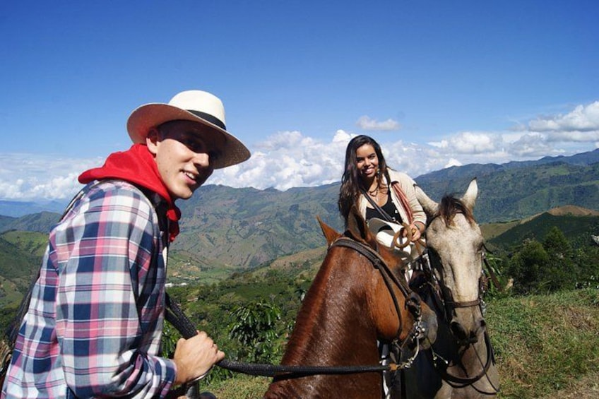 A person riding a horse on a mountain trail with a scenic view of green hills and a clear sky. 1