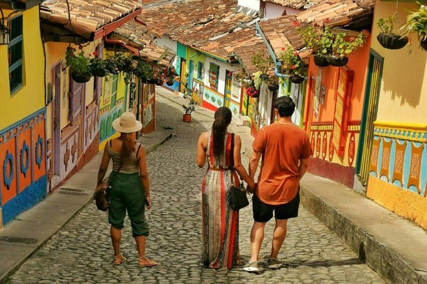 Una calle adoquinada bordeada de edificios coloridos, una persona con sombrero y una pareja caminando. 2
