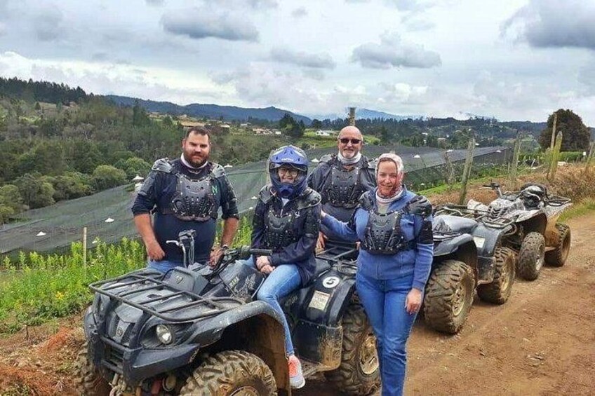 Quatre personnes à bord de quads dans un paysage rural, avec une rivière et des collines en arrière-plan. 1